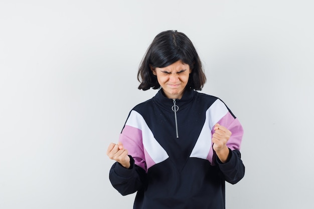 Petite fille montrant le geste du gagnant en chemise et à la chance, vue de face.