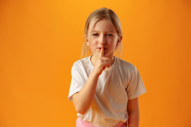 Petite fille montrant un geste de silence sur fond jaune