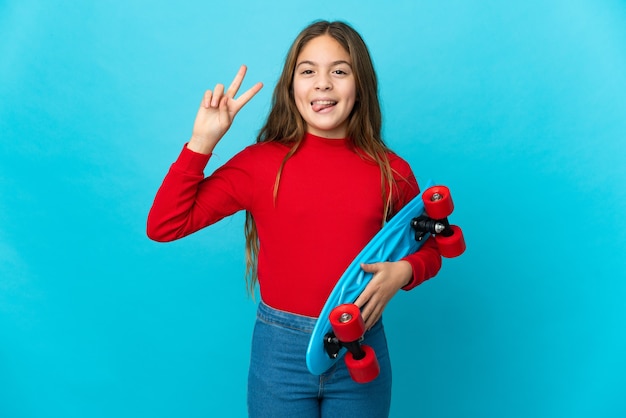 Petite fille sur un mur bleu isolé avec un patin avec une expression heureuse