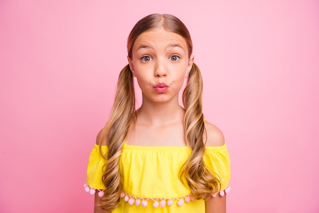 Petite fille avec des nattes posant contre le mur rose