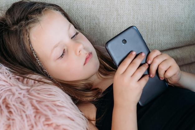 petite fille naviguant sur Internet ou regardant des vidéos sur téléphone mobile. invasion et surutilisation de la technologie moderne. problèmes d'éducation des enfants.