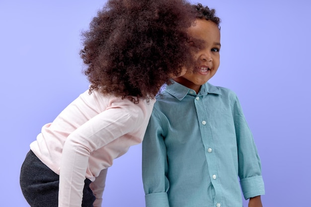 Petite fille noire embrassant son frère sur la joue isolé sur fond de studio violet enfants mignons dans