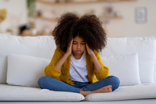 Petite fille noire stressée assise sur un canapé à la maison