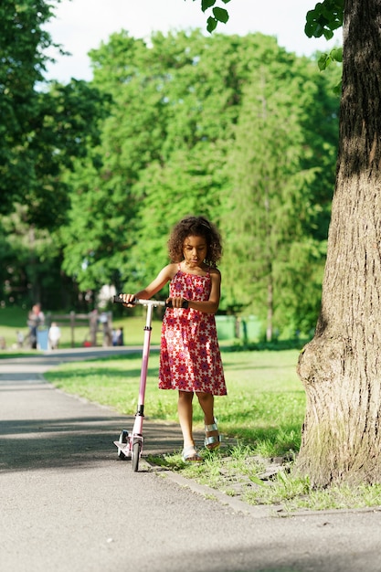 Photo petite fille noire avec une trottinette dans un parc de la ville