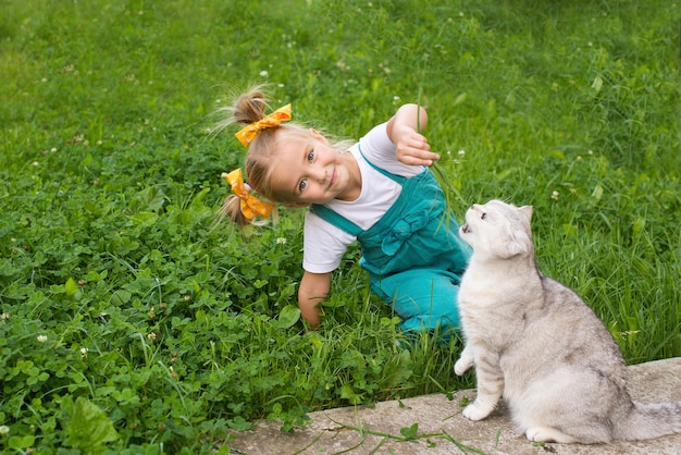 une petite fille nourrit un chat avec de l'herbe