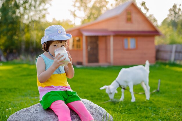 Une petite fille nourrit une chèvre sur la pelouse un été ensoleillé, dans un pays en Russie.