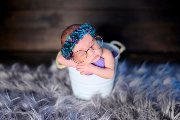 Une petite fille nouveau-née à l'intérieur d'un cube en métal blanc portant d'énormes lunettes et un bandeau de fleurs bleues