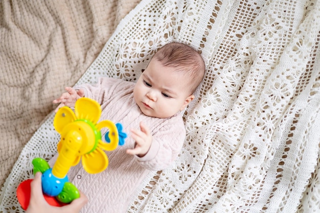 Une petite fille nouveau-née joue avec un hochet éducatif jaune vif à la maison dans la chambre de la chambre des enfants sur le lit Portrait en gros plan