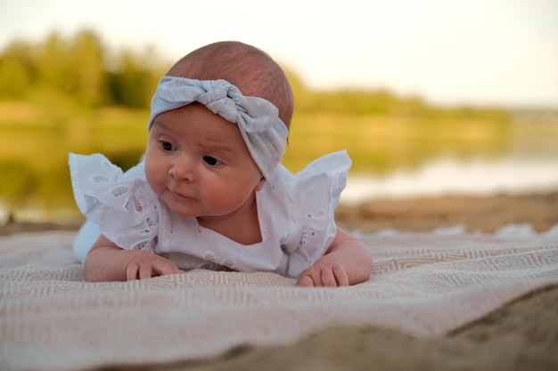 La petite fille nouveau-née se trouve sur la plage dans une robe blanche