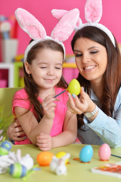 Petite fille avec des oeufs de peinture de mère pour des vacances de Pâques