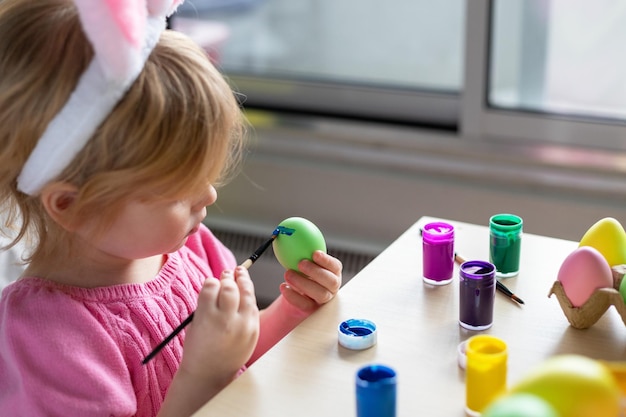 Petite fille avec des oreilles de lapin de Pâques peignant des œufs colorés Pâques fête familiale à la maison