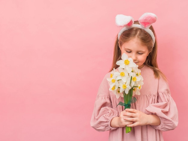 Petite fille avec des oreilles de lapin sentant des fleurs de narcisse sur fond rose