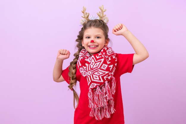 Une petite fille avec des oreilles de renne sur la tête et une écharpe de Noël danse.