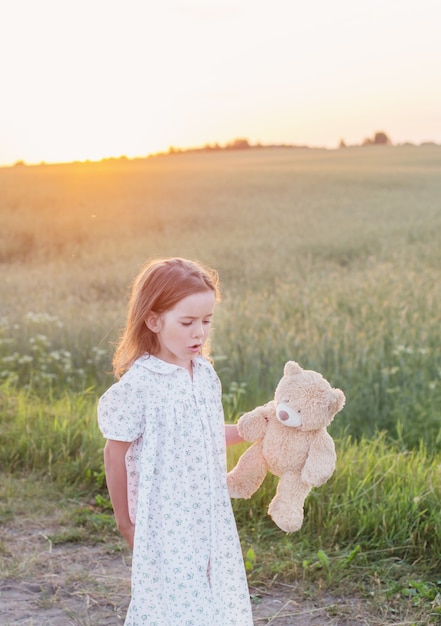 Petite fille avec ours en peluche sur route au coucher du soleil