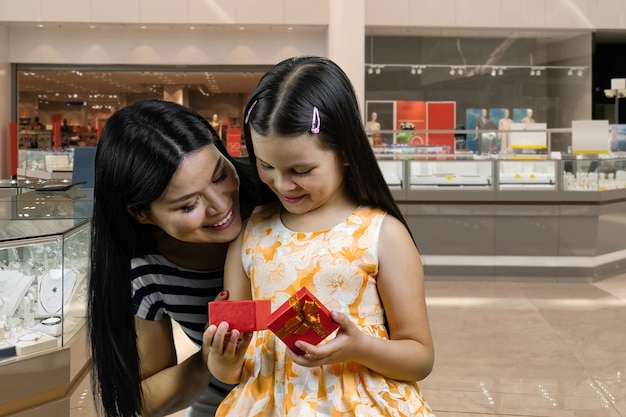 La petite fille ouvre une boîte-cadeau rouge de sa mère