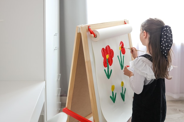 Une petite fille avec une palette dans ses mains dessine des fleurs sur un chevalet