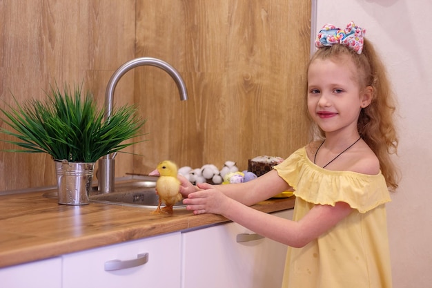 Une petite fille à Pâques avec de petits canetons jaunes à côté du gâteau et des oeufs peints Bonheur de famille de vacances
