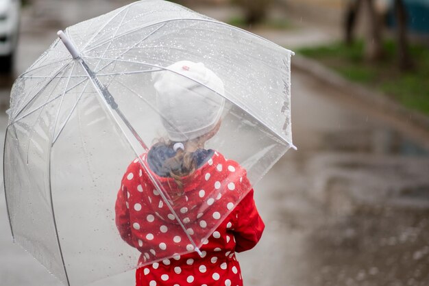 Une petite fille a un parapluie transparent dans ses mains. Pluie. Style de vie.