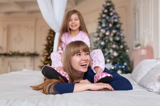 Petite fille passe du temps à jouer avec maman en position couchée dans son lit. Conte de Noël. Enfance heureuse.