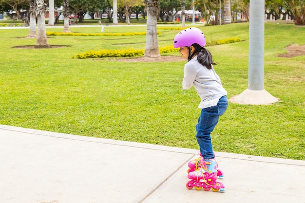 La petite fille patine avec ses patins à roulettes