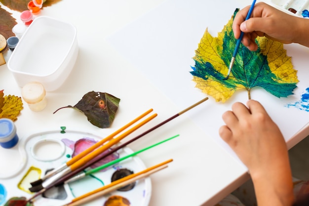 Petite fille peignant sur des feuilles jaunes d'automne à la gouache, arts pour enfants, créativité pour enfants, art d'automne.