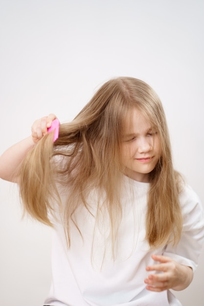 Petite Fille Peigne Les Cheveux Longs Et Emmêlés Sur Un Fond Blanc. Cosmétiques Pour Le Soin Des Cheveux Des Enfants.