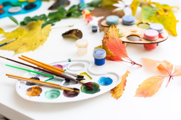 petite fille peint des feuilles avec un pinceau à la maison, art d'automne.