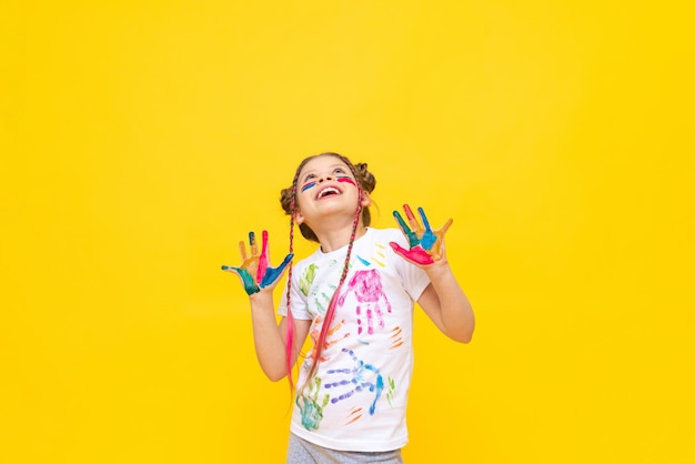 Une petite fille peinte avec des peintures regarde votre publicité sur un fond jaune isolé L'art de peindre avec des peintures pour enfants Cours d'art pour écoliers Espace de copie