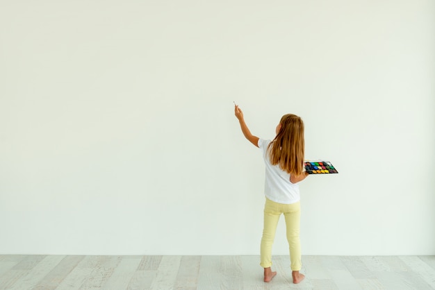 Petite fille peinture sur mur blanc à l'intérieur