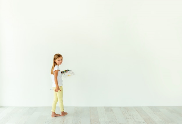 Petite fille peinture sur mur blanc à l'intérieur