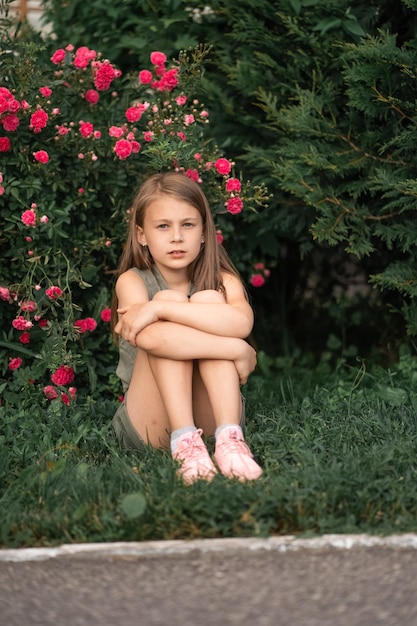 Petite fille pensive à l'extérieur assis près d'un rosier