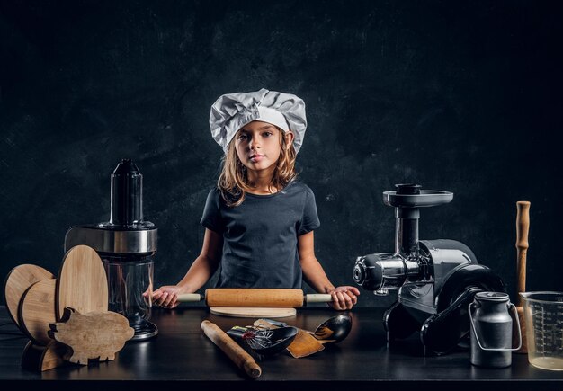 Une petite fille pensive en toque pose pour un photographe avec un équipement de cuisine.