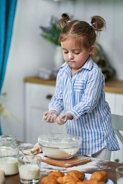 Petite fille pétrit la pâte dans la cuisine à la maison.