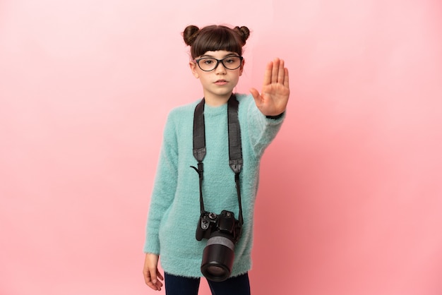 Petite fille photographe isolée sur mur rose faisant le geste d'arrêt