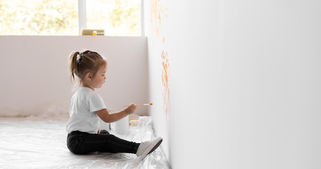 Une petite fille avec un pinceau dans les mains dessine sur le mur. Concept de rénovation domiciliaire.