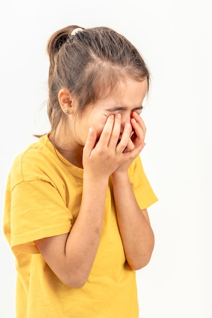 Une petite fille pleure en couvrant son visage avec ses mains sur un fond blanc