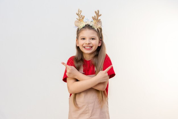 Une petite fille pointe deux doigts vers la publicité. cornes de Noël sur la tête d'un enfant.