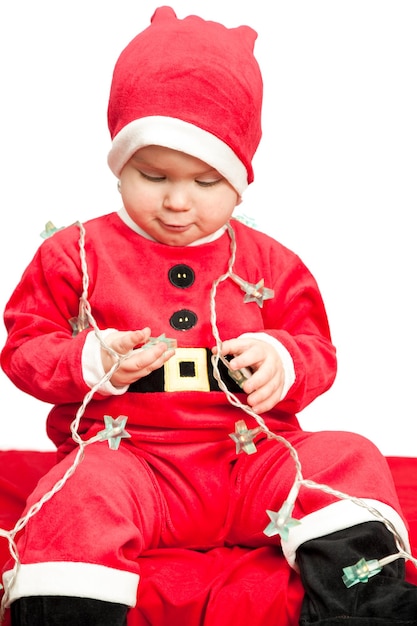 Petite fille portant le costume du Père Noël jouant avec les lumières de Noël sur fond blanc