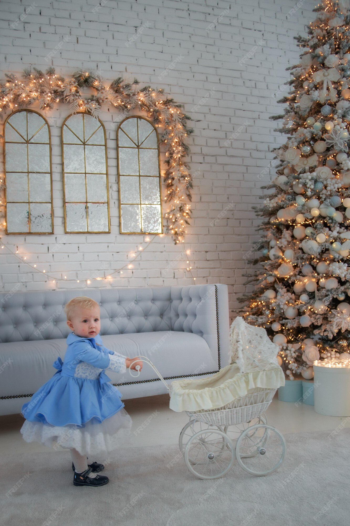 Une Petite Fille Portant Une Jolie Robe Et Un Bandeau Porte Une Poussette  Dans Une Pièce Décorée De Façon Festive Avec Une Guirlande De Lumières.