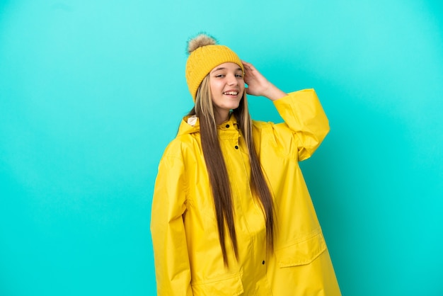 Petite fille portant un manteau imperméable sur fond bleu isolé souriant beaucoup