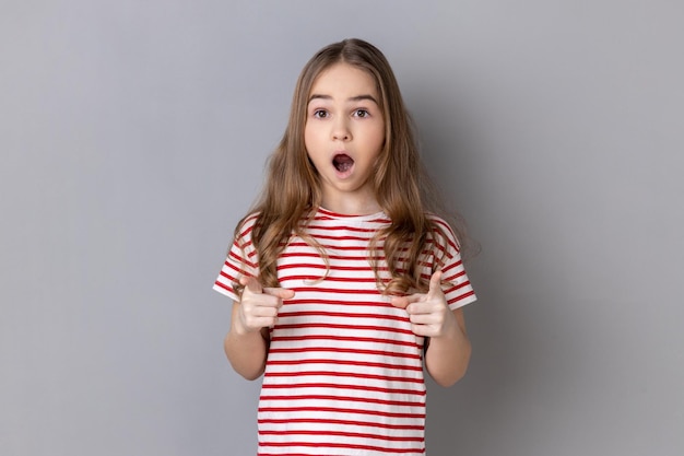 Petite fille portant un t-shirt pointant vers la caméra avec une expression choquée surprise et la bouche ouverte