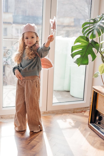 Petite fille porte des ailes roses une couronne une baguette magique et s'imagine une fée magique et joue à des jeux imaginaires à la maison