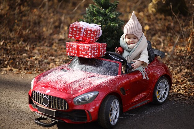 une petite fille porte un arbre de Noël et des cadeaux dans une voiture rouge