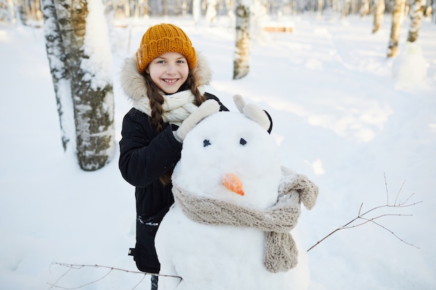 Petite fille posant avec bonhomme de neige