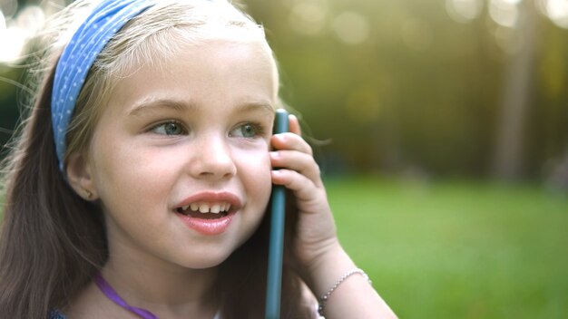 Petite Fille Positive Ayant Une Conversation Sur Son Téléphone Portable Dans Un Parc D'été.