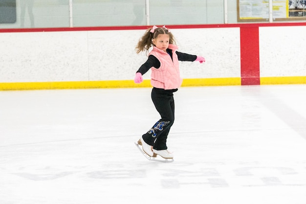 Photo petite fille pratiquant des mouvements de patinage artistique sur la patinoire intérieure