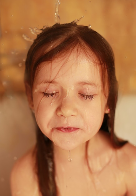 Une petite fille prend une douche L'eau coule dans les cheveux Les filles les yeux sont fermés