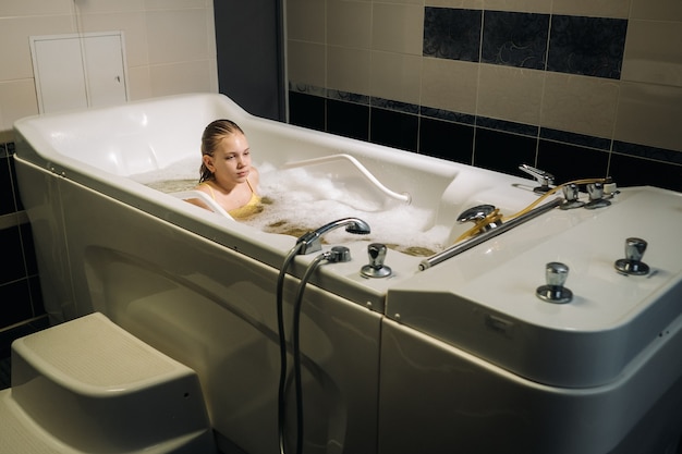 Une petite fille prend la procédure dans un bain minéral. Le patient reçoit des traitements à l'eau avec un bain de perles minérales.