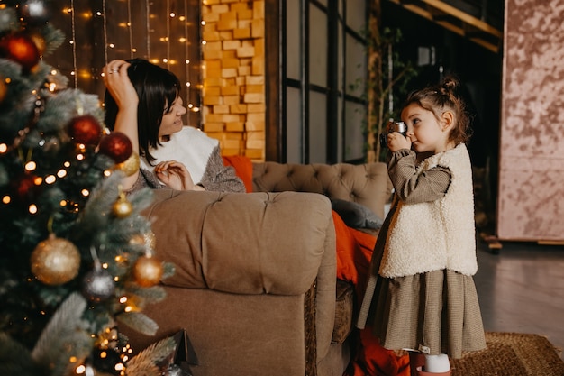 Petite fille à prendre des photos de sa mère à la maison, à côté d'un arbre de Noël