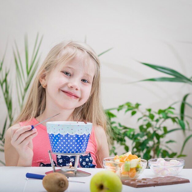 Petite fille prépare et mange une fondue au chocolat.